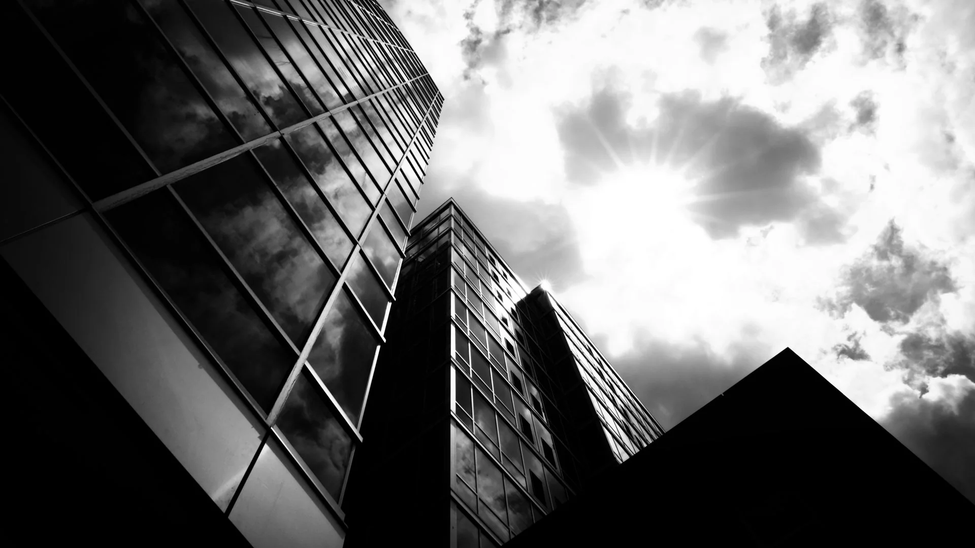 Low-angle black and white view of glass towers against a bright sky